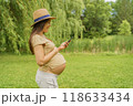 Pregnant woman om phone app reading about pregnancy or shopping baby clothing online. Portrait of happy smiling expectant mother in 3rd trimester in city park nature. Asian girl showing tummy belly 118633434