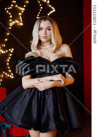 Blonde woman in black dress posing for photo in front of Christmas tree Blonde woman in black dress posing for photo in front of Christmas tree 118633551