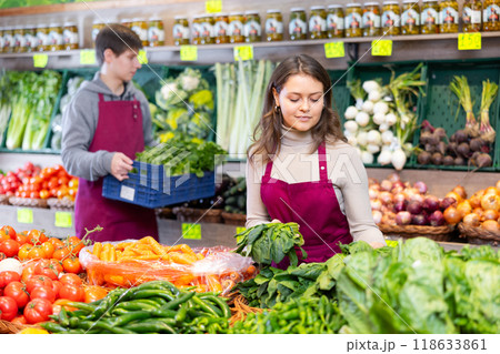 Young female seller placing bunch of spinach on counter in grocery market 118633861