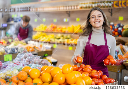 Saleswoman in an apron puts ripe tomatoes on supermarket window 118633888