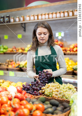 Young woman seller lays grapes on counter 118633948