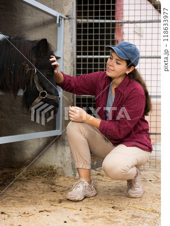 Portrait of woman farmer standing near pony at stable 118633977