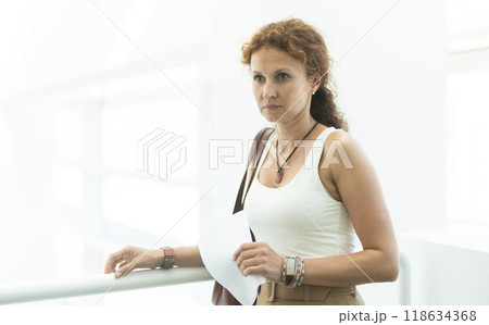 Middle-aged woman standing at handrails in public building Middle-aged woman standing at handrails in public building 118634368