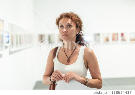 Middle-aged woman looking at pictures on wall in museum Middle-aged woman looking at pictures on wall in museum 118634437