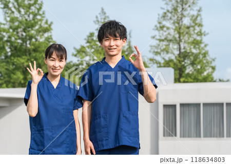病院・施設の前にいるスクラブをきた医療従事者の男女スタッフ(作業療法士・看護師) 病院・施設の前にいるスクラブをきた医療従事者の男女スタッフ(作業療法士・看護師) 118634803