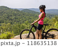Woman on electric mountain bike in pink top, helmet and sunglasses, enjoying scenic forest view. eMTB concept 118635138