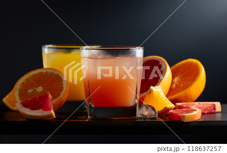 Glasses of grapefruit and orange juice with ice on a black background. 118637257