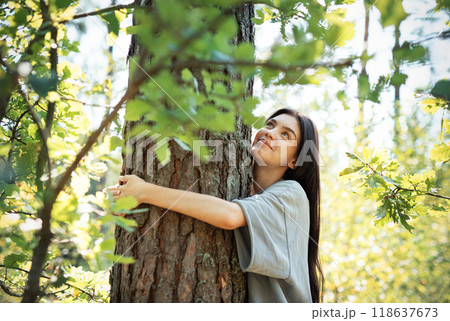 Young woman embracing a tree while enjoying nature in a sunlit forest during summer Young woman embracing a tree while enjoying nature in a sunlit forest during summer 118637673