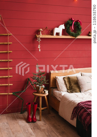 Red bedroom with a Christmas tree and a wreath on the wall. Bed is covered with a white comforter and pillows 118638760