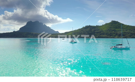 Sailboats anchored in turquoise lagoon, green mountains tropical island in background. Crystal clear water reflects blue sky. Yacht catamaran boat tour to French Polynesia. Exotic summer luxury travel 118639717