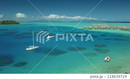 Two sailboats yachts anchor near shallow turquoise water lagoon near tropical island, luxury resort overwater bungalows in background. Maldives remote wild nature paradise, exotic summer luxury travel Two sailboats yachts anchor near shallow turquoise water lagoon near tropical island, luxury resort overwater bungalows in background. Maldives remote wild nature paradise, exotic summer luxury travel 118639729