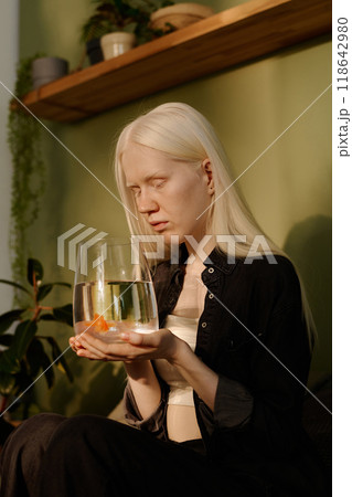 Vertical shot of gen Z girl with albinism holding small aquarium in hands and looking at her pet goldfish Vertical shot of gen Z girl with albinism holding small aquarium in hands and looking at her pet goldfish 118642980
