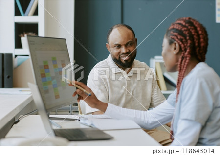 Two professionals discussing work tasks at an office desk while viewing digital charts on a monitor Clients or colleagues collaborating and sharing ideas in workplace Two professionals discussing work tasks at an office desk while viewing digital charts on a monitor Clients or colleagues collaborating and sharing ideas in workplace 118643014