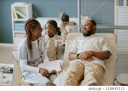 Medical professional consulting and discussing health concerns with patient and child in modern clinic setting. Clinic backdrop including medical equipment and documents 118643111