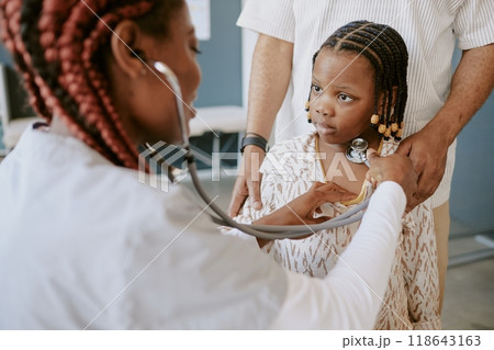Medical professional using stethoscope during examination of young girl in clinic setting showing concentration and thoroughness in health evaluation 118643163