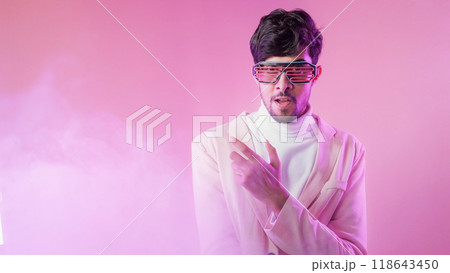 Disco party. Cyber fashion. Eyewear accessory. Purple neon light confident man in glasses posing in color smoke cloud isolated on pink empty space background. Disco party. Cyber fashion. Eyewear accessory. Purple neon light confident man in glasses posing in color smoke cloud isolated on pink empty space background. 118643450
