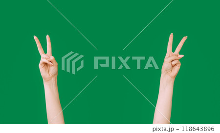 Victory sign. Peace gesture. Friendly greeting. Female hands showing two fingers signal isolated on green empty space background. Victory sign. Peace gesture. Friendly greeting. Female hands showing two fingers signal isolated on green empty space background. 118643896