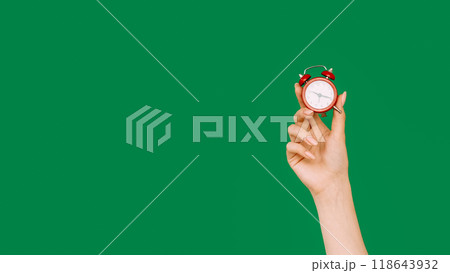 Hurry up. Time reminder. Last minute offer. Female hand showing hour on vintage miniature red alarm clock isolated on green empty space background. Hurry up. Time reminder. Last minute offer. Female hand showing hour on vintage miniature red alarm clock isolated on green empty space background. 118643932