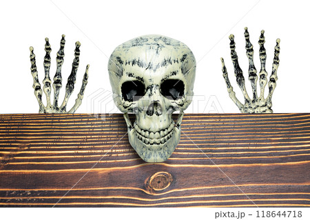 The human skeleton is sitting on a wooden table with its scary smile on a white background. The human skeletons, devil, evil, or satan seem to be watching or waiting for something. The scene is eerie The human skeleton is sitting on a wooden table with its scary smile on a white background. The human skeletons, devil, evil, or satan seem to be watching or waiting for something. The scene is eerie 118644718