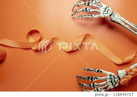 A skeleton hand with an orange ribbon with a white polka dot design. The skeleton is positioned on an orange background 118644727