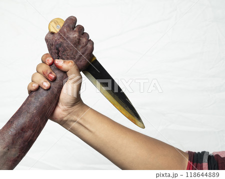 A zombie hand with a bloody wound fighting with a man isolated over a white background. A zombie hand holding a knife and the man holding a zombie hand. The knife is pointed at the man hand, creating A zombie hand with a bloody wound fighting with a man isolated over a white background. A zombie hand holding a knife and the man holding a zombie hand. The knife is pointed at the man hand, creating 118644889