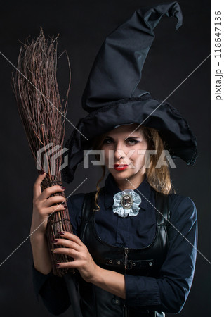 Beautiful witch in a hat and with a broom on a black background 118647136
