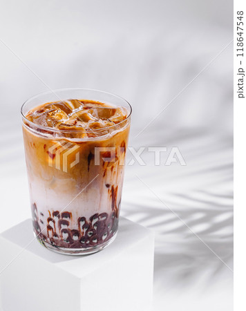 Iced coffee latte with chocolate syrup standing on white cube with tropical leaf shadow 118647548