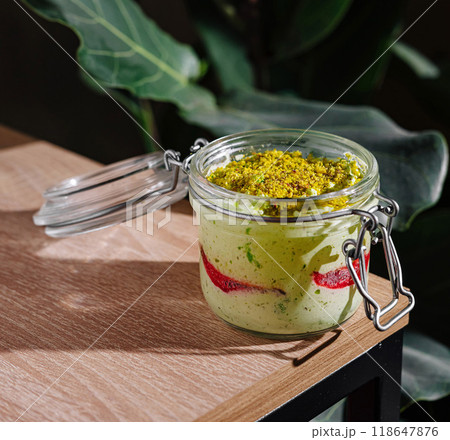 Delicious pistachio dessert with red fruit jelly in a glass jar standing on wooden table 118647876