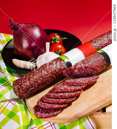 Sliced sausage on cutting board with onion, garlic and tomatoes on red background 118647969