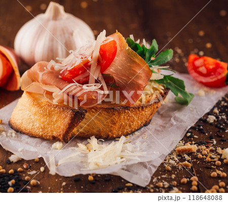 Delicious bruschetta with parma ham, cheese, tomatoes and arugula on wooden table Delicious bruschetta with parma ham, cheese, tomatoes and arugula on wooden table 118648088