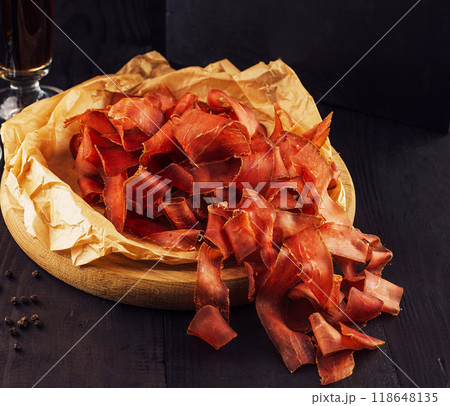 Sliced ??dried beef basturma served on a wooden plate on a black background Sliced ??dried beef basturma served on a wooden plate on a black background 118648135