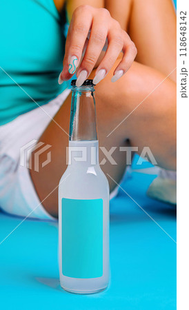 Woman opening bottle of refreshing cold drink with blank label on blue background 118648142