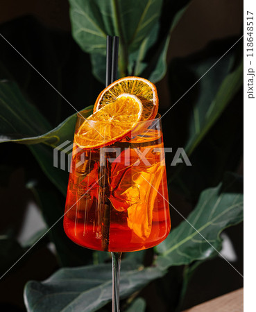 Refreshing aperol spritz cocktail standing on a table with tropical plants in the background 118648517