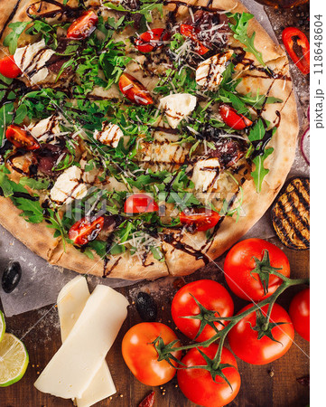 Freshly baked pizza lying on table with ingredients spread around 118648604