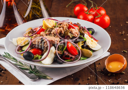 Fresh nicoise salad with tuna on a wooden table being prepared with eggs and tomatoes around 118648636