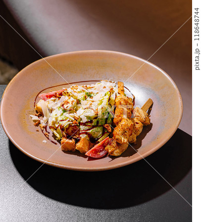Delicious caesar salad with chicken skewers served on plate in restaurant Delicious caesar salad with chicken skewers served on plate in restaurant 118648744