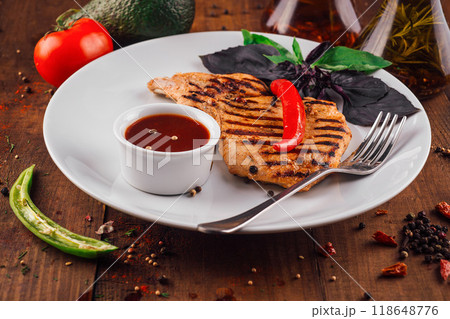 Grilled chicken breast with tomato sauce served on white plate on wooden table Grilled chicken breast with tomato sauce served on white plate on wooden table 118648776