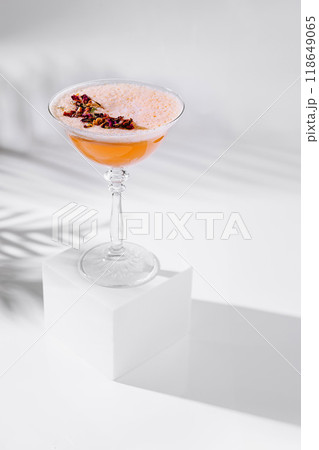 Cocktail glass standing on white cube with tropical leaf shadow 118649065