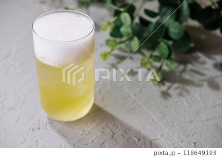 Glass of cold cocktail with foam on white table background with green leaves 118649193