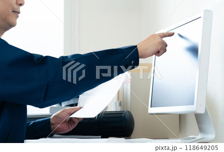 パソコンと資料を見比べる作業着の男性 118649205