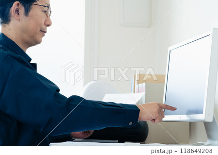パソコンと資料を見比べる作業着の男性 パソコンと資料を見比べる作業着の男性 118649208