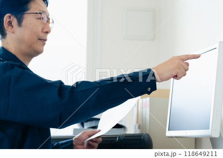 パソコンと資料を見比べる作業着の男性 118649211
