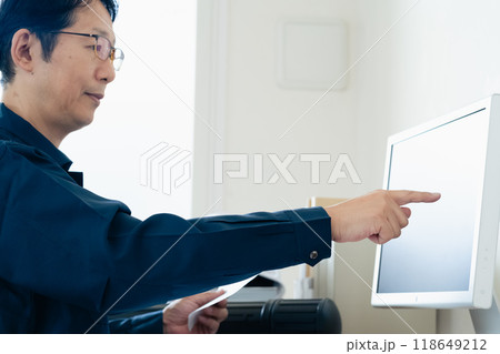 パソコンと資料を見比べる作業着の男性 パソコンと資料を見比べる作業着の男性 118649212
