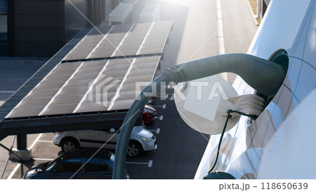 Electric car is charging from a charging station that takes energy from solar panels. Close up. Electric car is charging from a charging station that takes energy from solar panels. Close up. 118650639