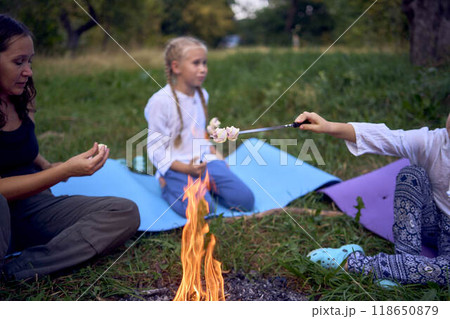 mother and her daughters roasting and eating marshmallows on the campfire, camping vacation with children, mosquito bites on children's faces mother and her daughters roasting and eating marshmallows on the campfire, camping vacation with children, mosquito bites on children's faces 118650879