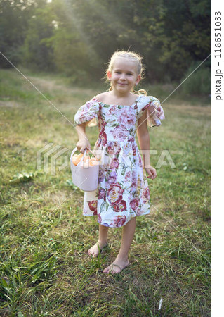 little blond girl with braids in a floral dress with a basket on an Easter egg hunt 118651033