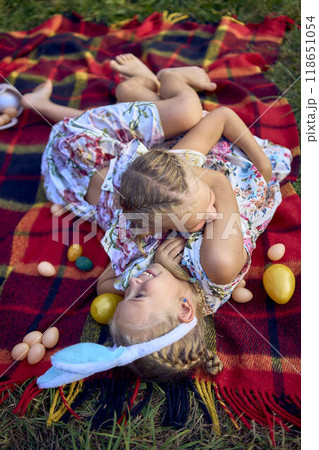 little girls, sisters, playing on a picnic blanket with eggs after an Easter egg hunt 118651054
