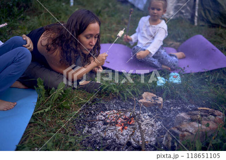 mother and her daughters  roasting and eating marshmallows on the campfire, camping vacation with children, mosquito bites on children's faces 118651105