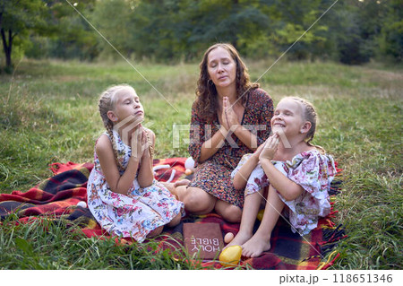 a mother and her two daughters read the holy bible and pray at an Easter picnic 118651346