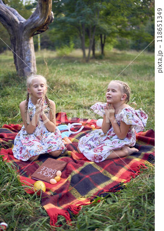 little girls sisters pray to god at easter picnic in garden little girls sisters pray to god at easter picnic in garden 118651349